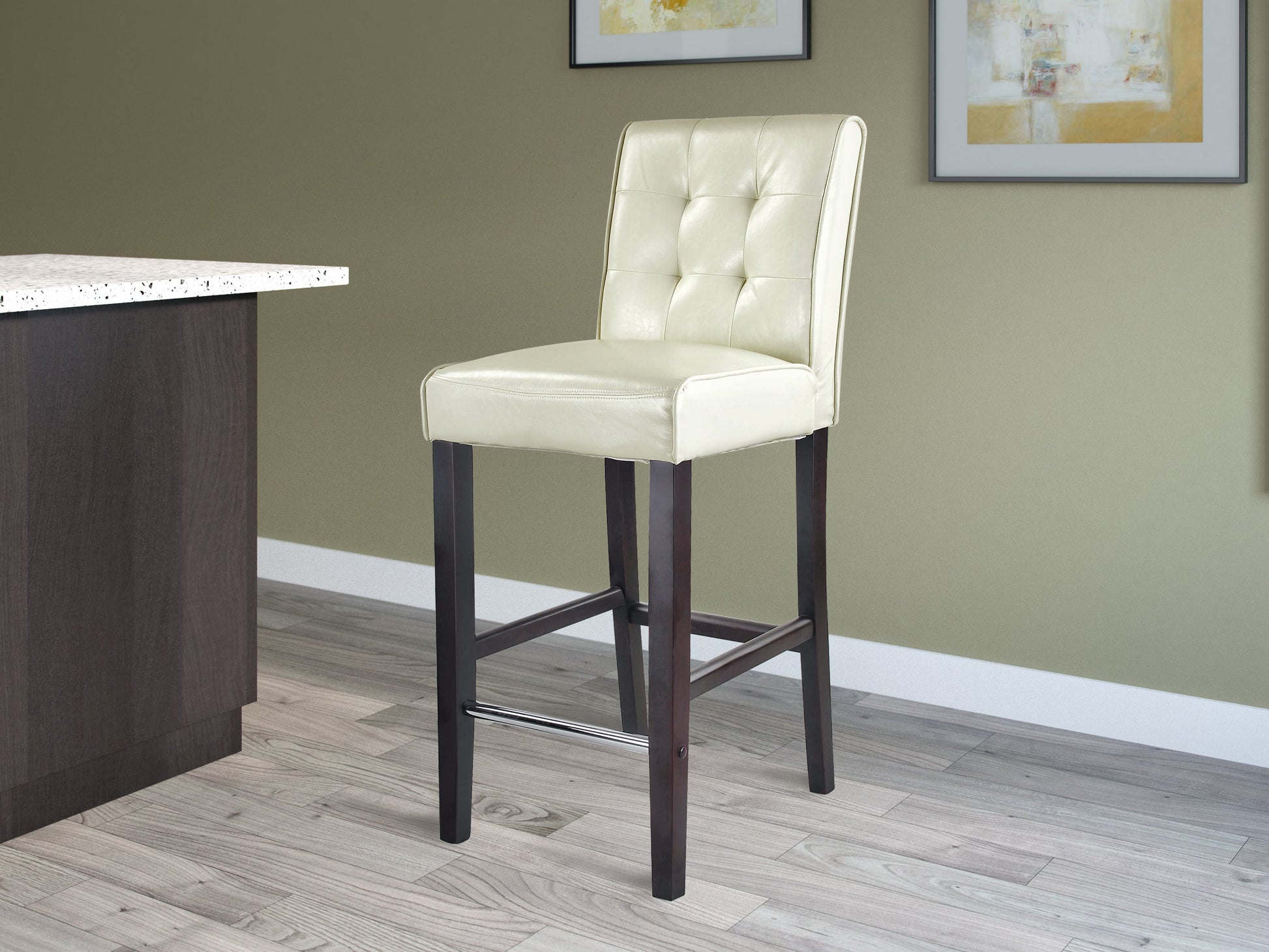 Cream bar height bar stool with padded seat, wooden legs, and a footrest. Upholstered in smooth cream fabric, featuring a modern design suitable for kitchen islands and home bars.