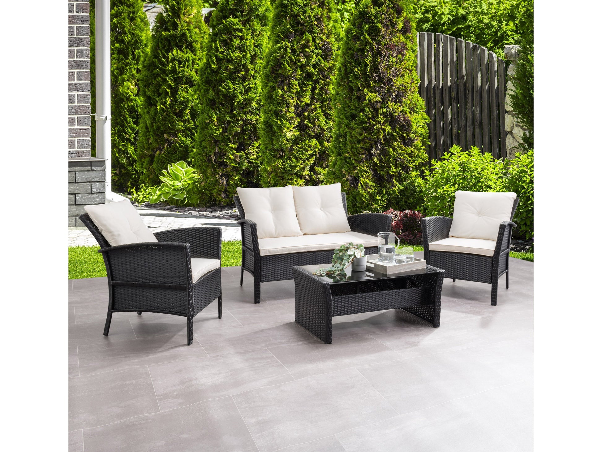 4-piece wicker patio conversation set in black and warm white, featuring a loveseat, two armchairs, and a glass-top coffee table with comfortable cushions and weather-resistant materials.