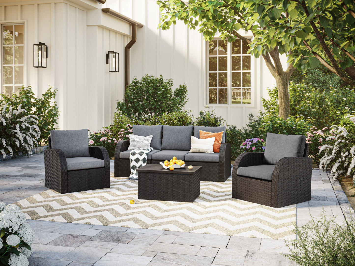 Grey outdoor patio conversation set with six pieces, including a modern sofa, two armchairs, a coffee table, and two ottomans. Features weather-resistant wicker, plush grey cushions, and a sleek tempered glass tabletop.